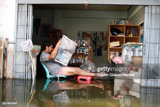 Man tries to read a newspaper in the as he sits amidst his flooded shop in the Wijit Kolnimit Community of Bangkok, This area, the Pasi Charoen...