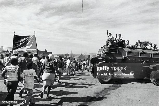 Armed South African police, on an armored Casspir vehicle, watch the procession of mourners carrying the banned African National Congress flag at the...