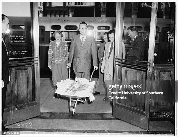 Pennies hauled to bank in wheelbarrow by vice president and employee of Pacific Mutual, Lyman P Robertson, Vice President, Helen Olson, George B...