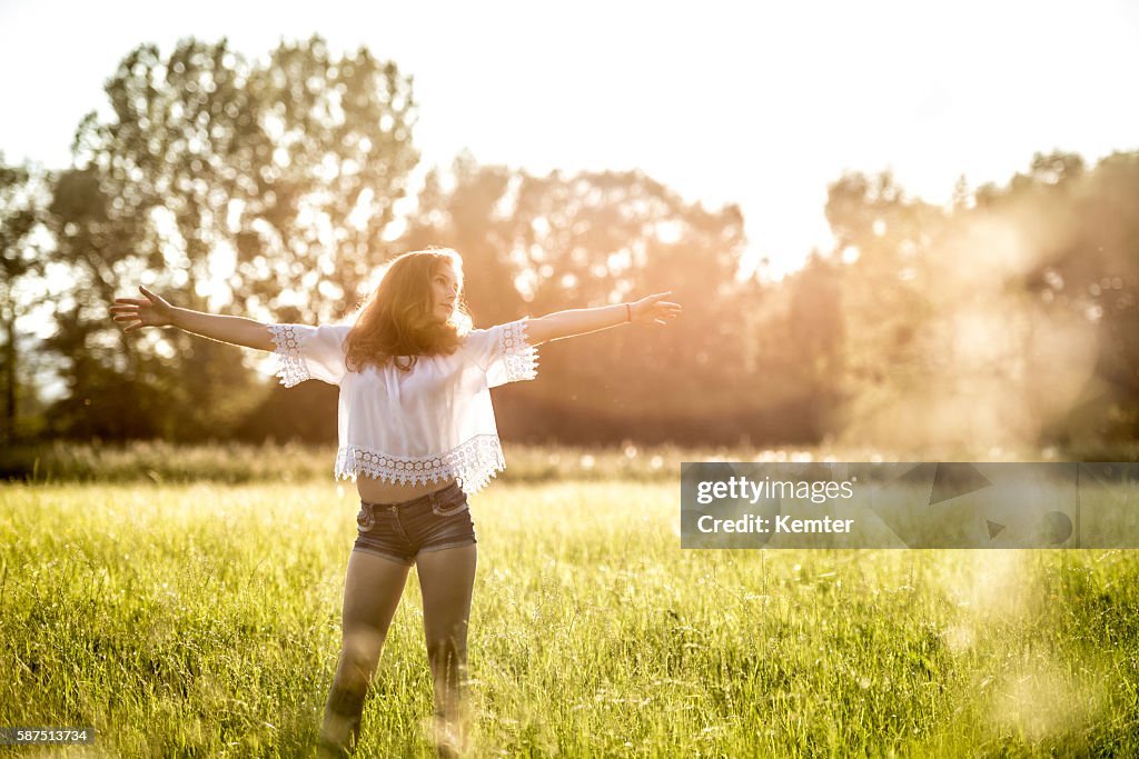 Teenage girl standing with arms outstretched in meadow