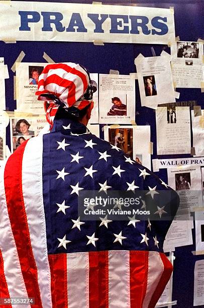 Three days after the terrorist attack on the World Trade Center, a New Yorker draped in the American flag, studies the messages and photographs...