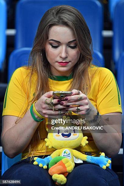 Fan of Brazil, with the Olympic mascot onto her lap, checks her mobile phone prior to a Men's round Group B basketball match between Spain and Brazil...