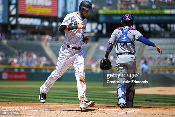 David Dahl of the Colorado Rockies crosses home plate on a single off the bat of Nolan Arenado as catcher Robinson Chirinos of the Texas Rangers...