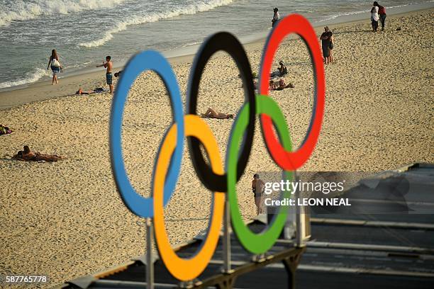 People are pictured walking along Copacaba beach through a set of Olympic rings, from during the men's beach volleyball qualifying match between...