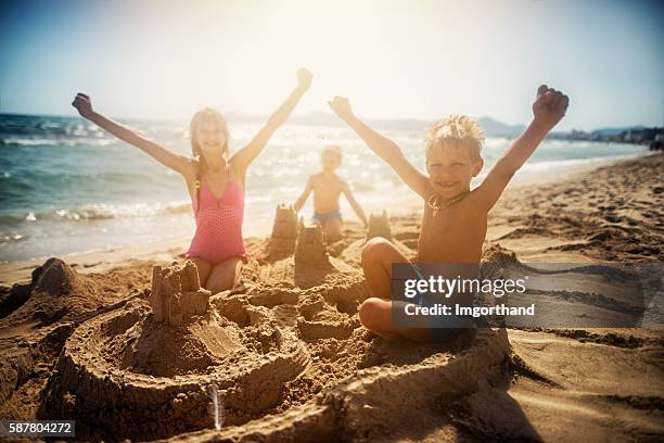 kinder bauen eine sandburg an einem schönen strand - kind sandburg stock-fotos und bilder