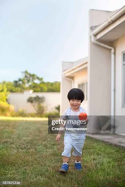 asian toddler 2 to 3 years boy playing kicking ball in the garden. - korea soccer stock-fotos und bilder