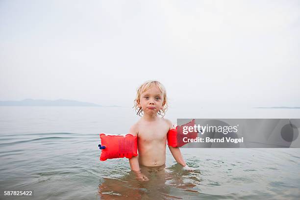 little boy (3-4) with water wings swimming - brazaletes acuáticos fotografías e imágenes de stock