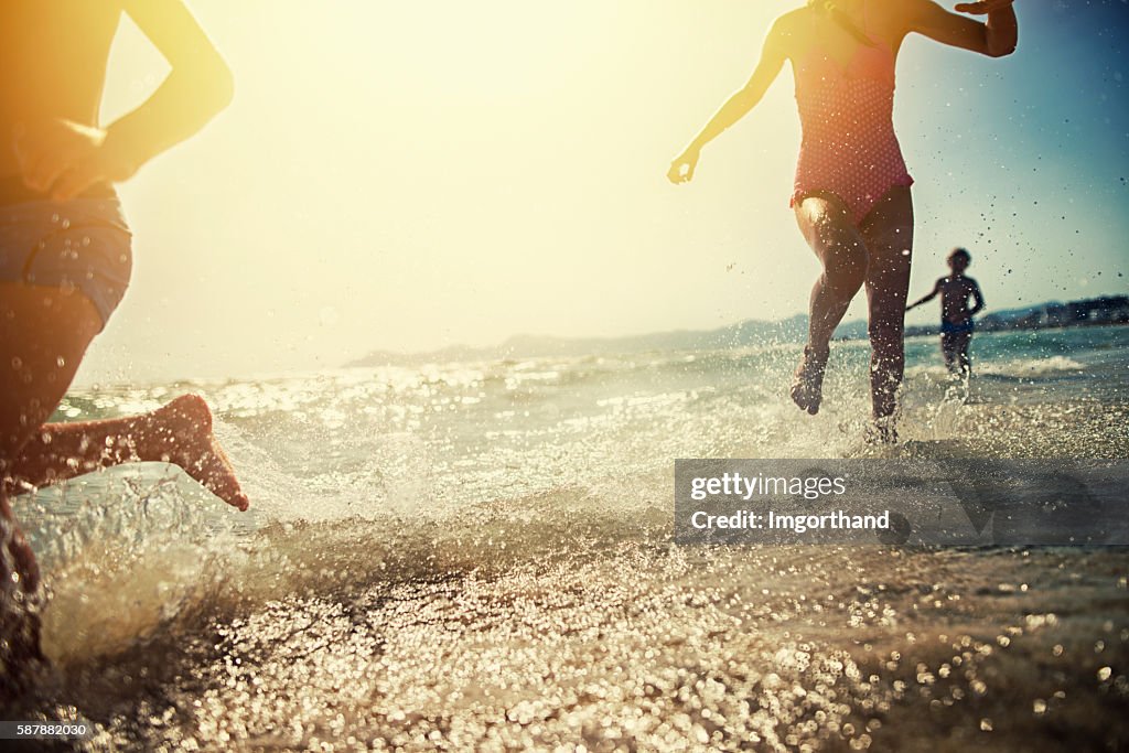 Brothers and sister running on beach on sunset