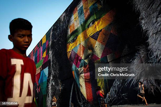 People walk in front of a section of a mural depicting an indigenous face created by Brazilian graffiti artist Eduardo Kobra along Olympic Boulevard...