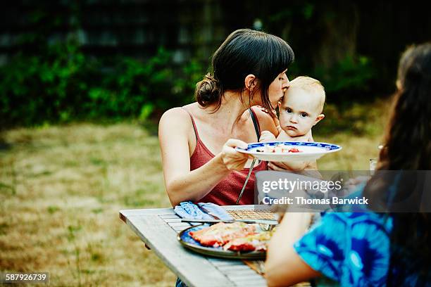 mother kissing daughter on head during barbecue - head on table stock-fotos und bilder