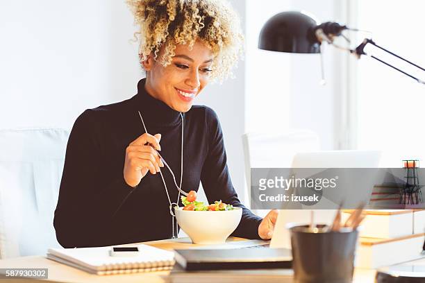 afro giovane donna americana che pranza alla scrivania - pranzo foto e immagini stock