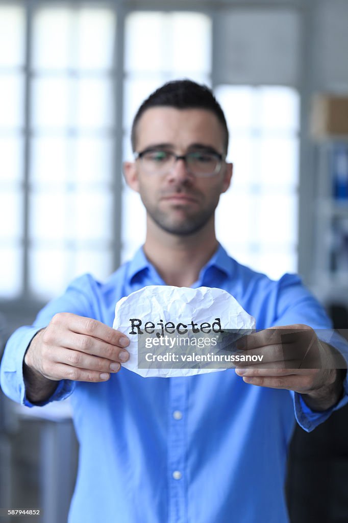 Sad young man holding a paper with sign "rejected"