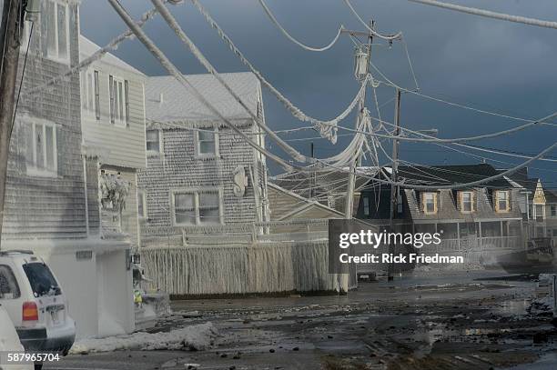 Water runs down the flooded streets as homes and power lines are covered in ice from the ocean spray during the a Nor'easter winter storm in...