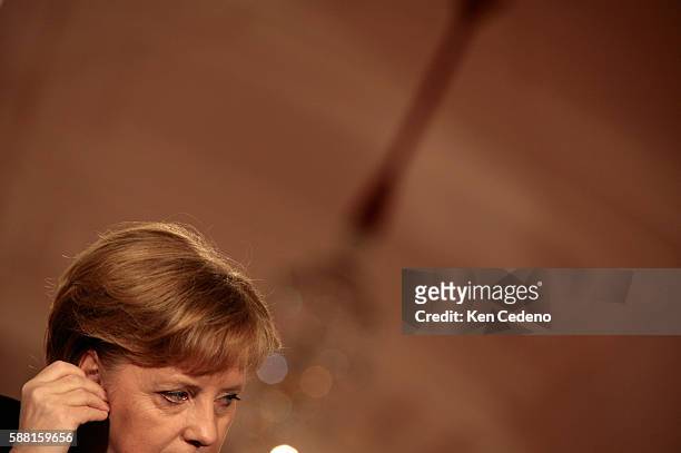 German Chancellor Angela Merkel, adjusts her ear piece as she listens to President George W. Bush during a joint press conference at The White House....