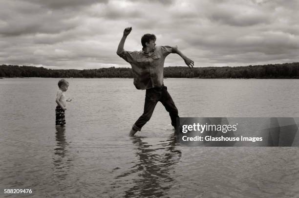 man skipping stones in lake with young boy standing behind - uncle nephew stock pictures, royalty-free photos & images