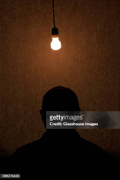 man sitting under light bulb, silhouette - interrogatório imagens e fotografias de stock