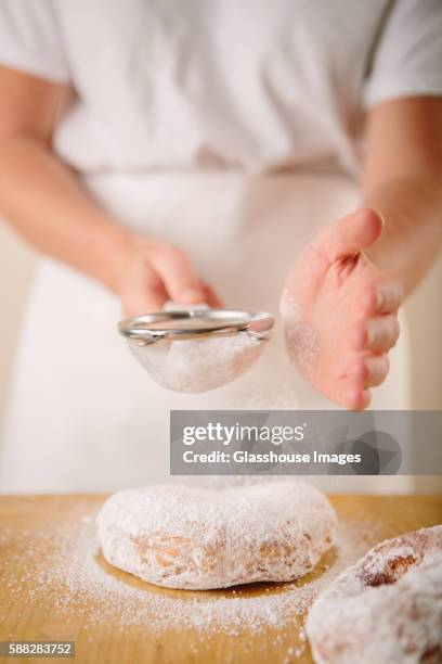 woman sprinkling powdered sugar on doughnuts - azúcar en polvo fotografías e imágenes de stock