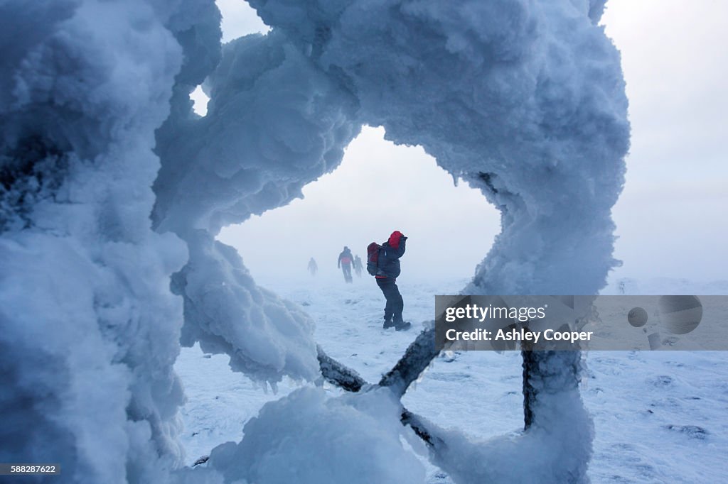 Mountaineers struggle through storm force winds to approach the summit of Cairngorm, seen through rime ice coating the automatic weather station, Scotland, UK.