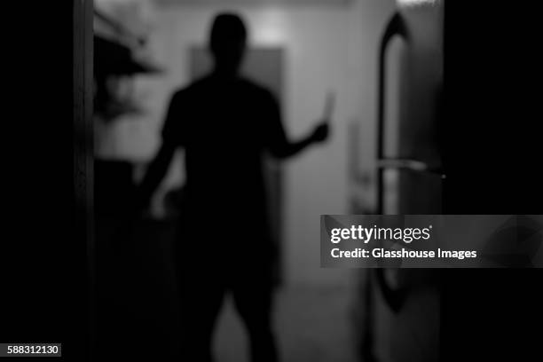 man holding knife in kitchen, rear view, silhouette - knife weapon stock-fotos und bilder