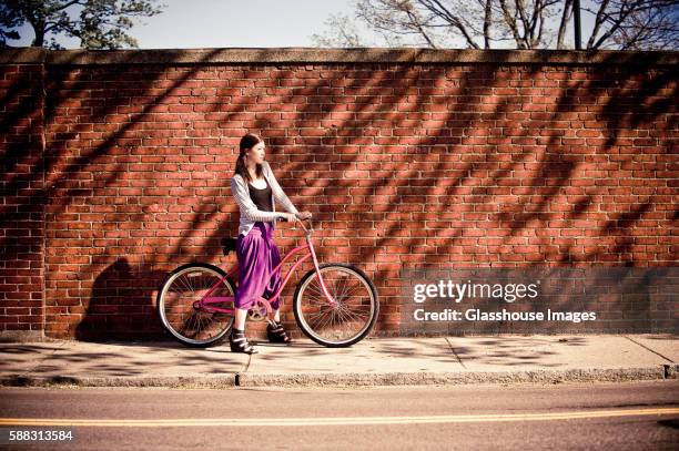 young woman in purple skirt with bicycle on sidewalk against brick wall - lila kjol bildbanksfoton och bilder