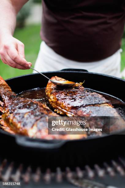 fish in cast iron pan being basted and cooked on grill - bañar en su jugo durante la cocción fotografías e imágenes de stock