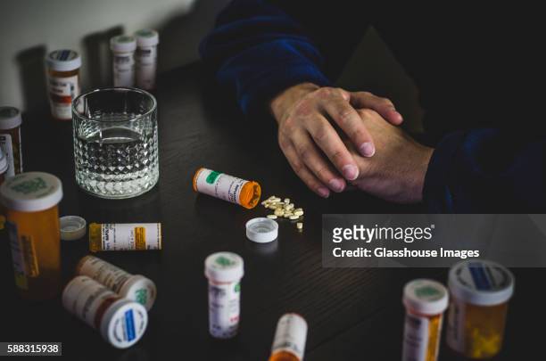 hands of man in robe surrounded by prescription pill bottles - mann tabletten stock-fotos und bilder