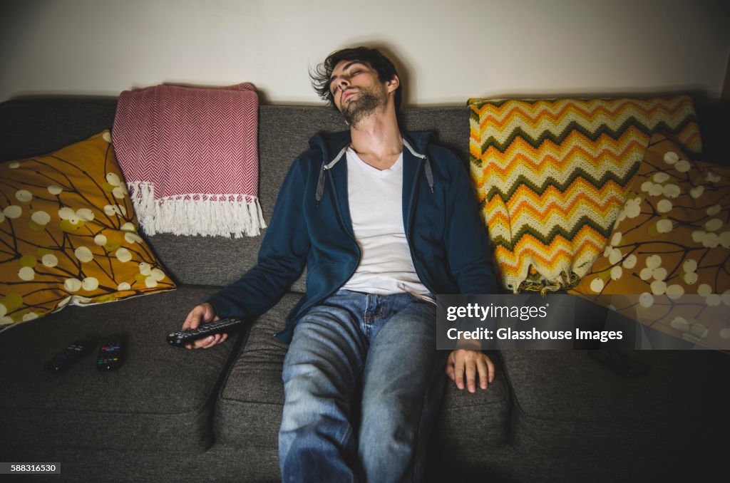 Young Adult Man Sleeping on Couch with TV Remote in Hand