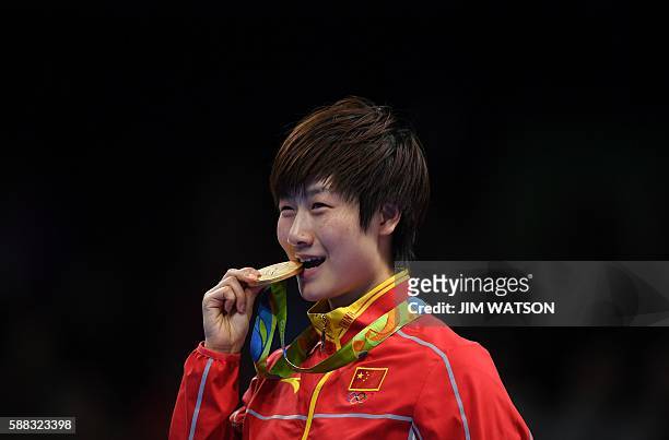 China's Ding Ning bites her gold medal after beating China's Li Xiaoxia in their women's singles final table tennis match at the Riocentro venue...