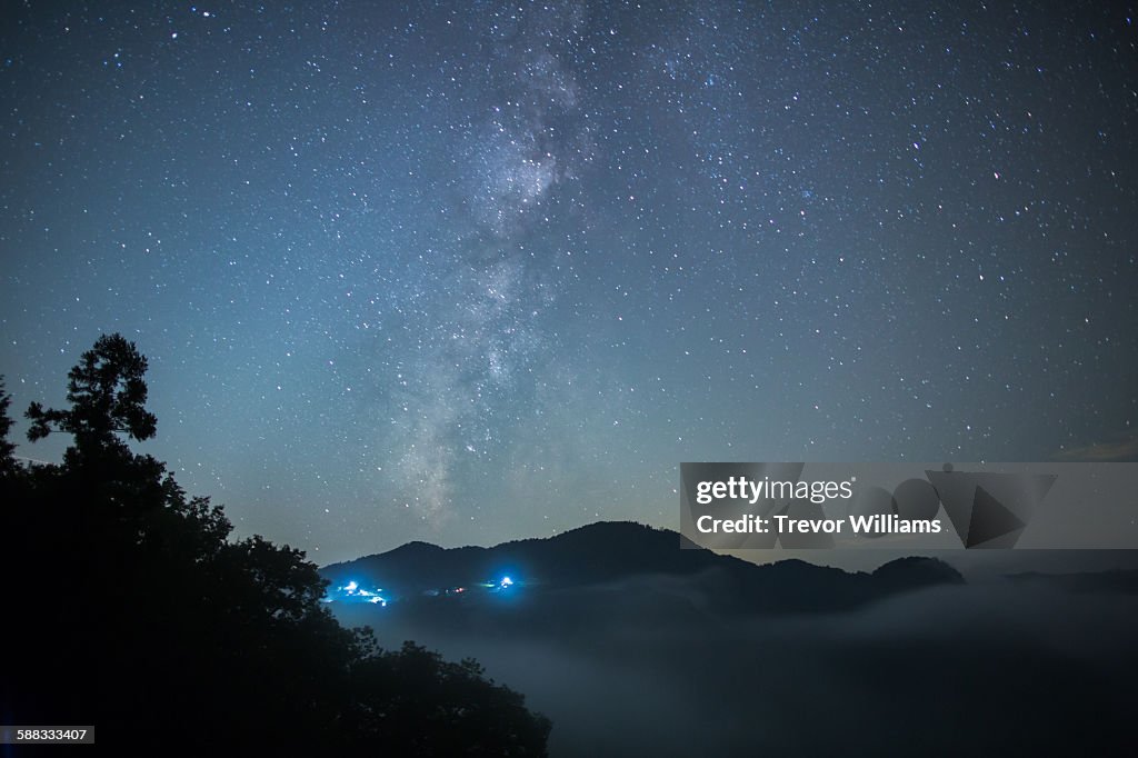 The Milky Way hangs about a valley filled with fog