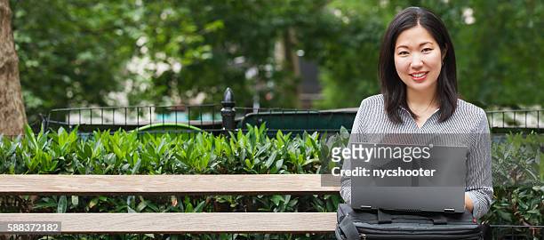 young asian businesswoman sitting on park bench working on laptop - mid adult women stock pictures, royalty-free photos & images