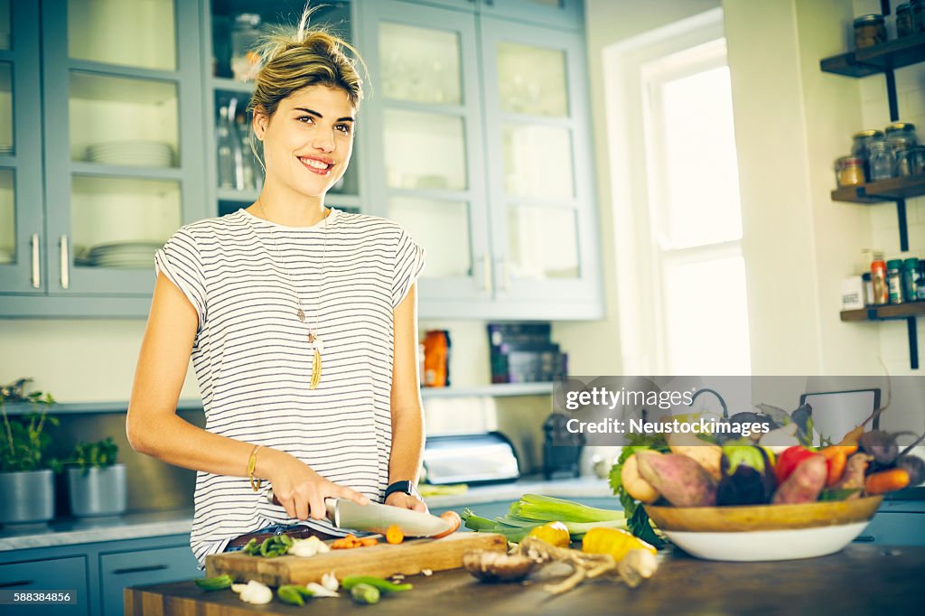 Thoughtful woman smiling while cutting carrot in kitchen