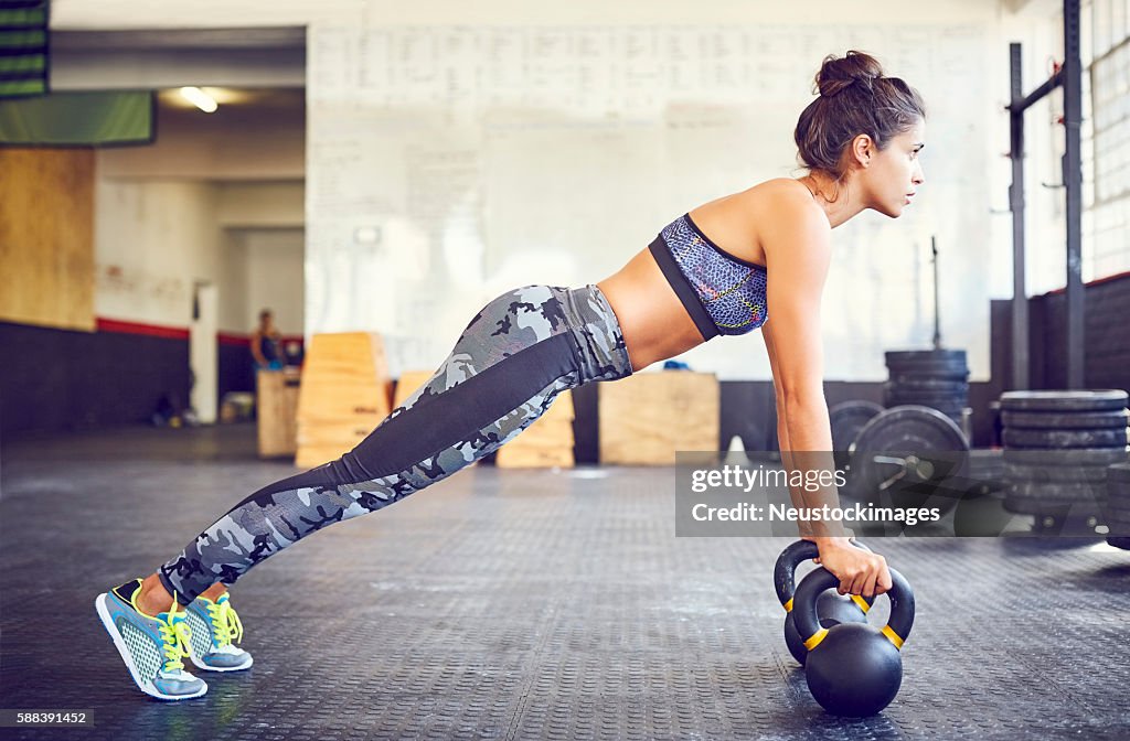 Determined fit athlete doing push-ups on kettlebells in gym