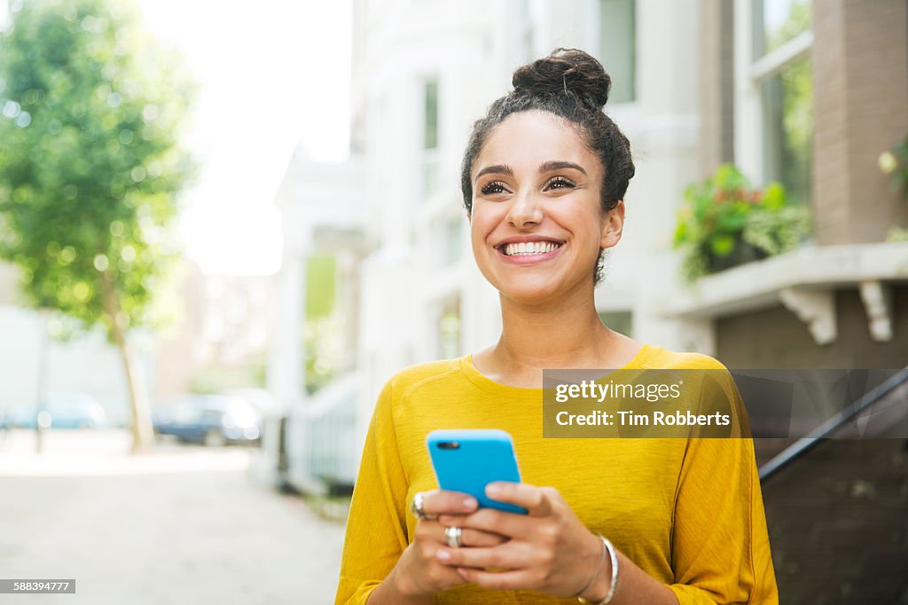 Happy woman with smart phone on street.
