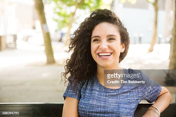 woman sat on bench smiling. - one young woman only photos fotografías e imágenes de stock