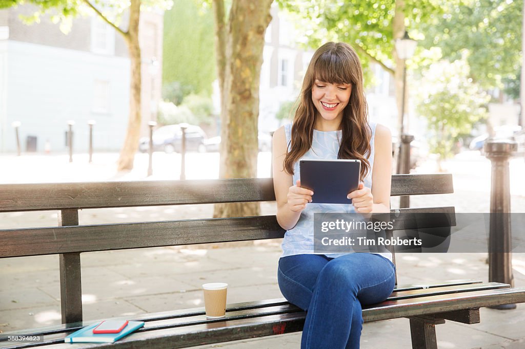 Woman sat on bench with tablet.