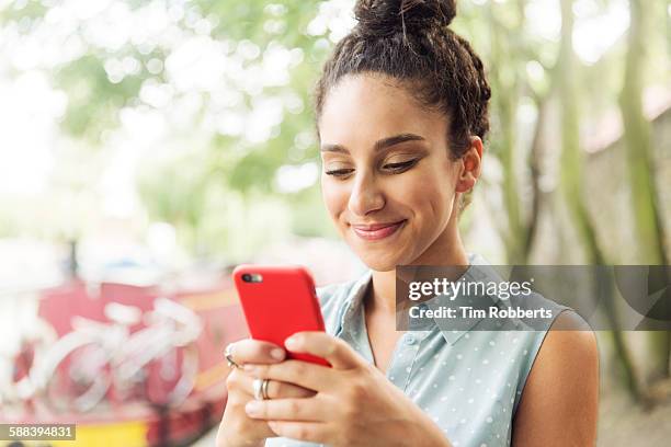 woman using smart phone next to river. - woman smiling park summer stock-fotos und bilder