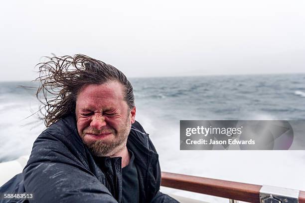 spray and sleet lashes the face of a man on a speeding boat in a storm. - funny man stock pictures, royalty-free photos & images