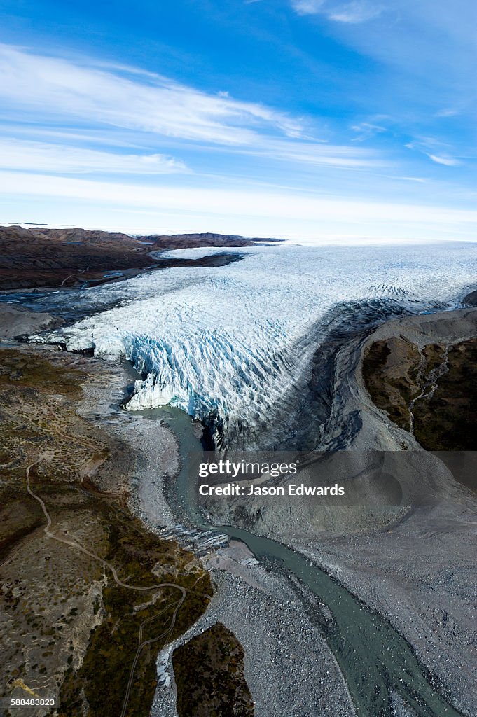 A river of meltwater flows from an enormous glacier into a floodplain.
