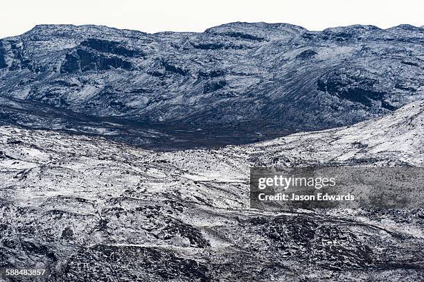 a dusting of snow covers barren and inhospitable mountain peaks on a highland tundra plateau. - snowfield fotografías e imágenes de stock
