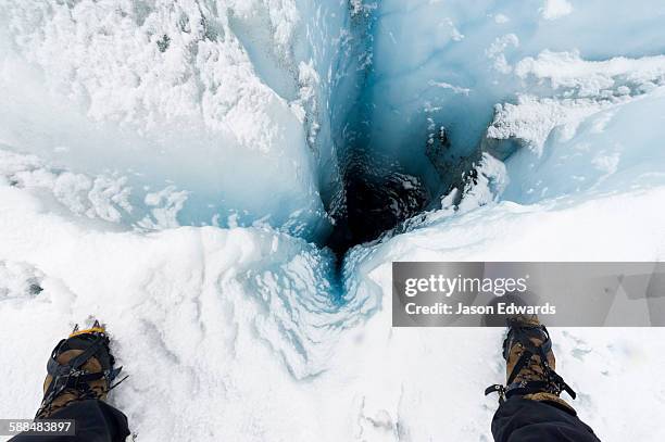 a hiker stands over a moulin, a narrow, tubular chute or crevasse through which water enters a glacier from the surface. - ice sheet stock pictures, royalty-free photos & images