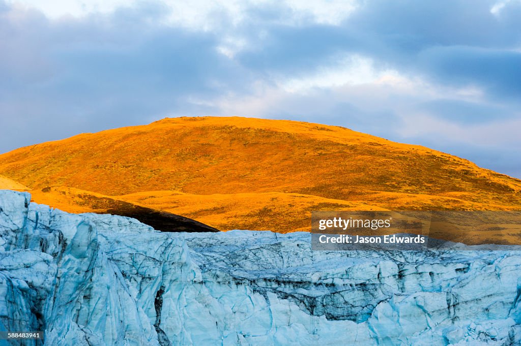 Sunset turns the exposed summit of a mountain orange above a glacier fracture zone.