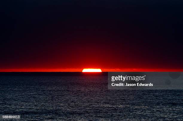 a slither of sunlight pierces a storm cloud above a darkened ocean at sunset. - splitter stock-fotos und bilder