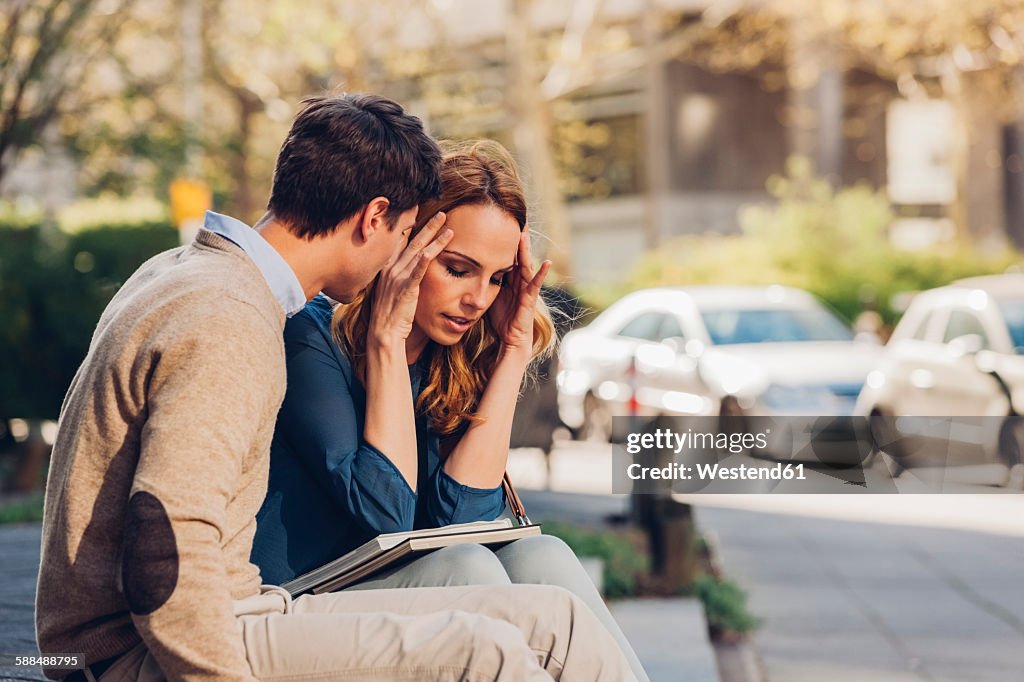 Couple sitting outdoors with woman holding head in hands