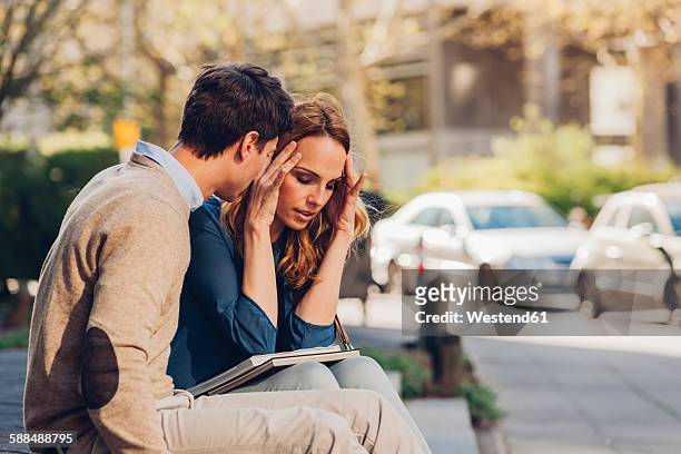 couple sitting outdoors with woman holding head in hands - streiten stock-fotos und bilder