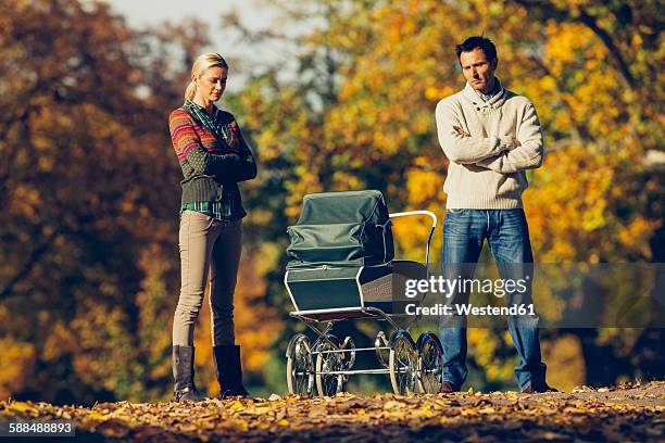 reserved couple standing with crossed arms looking at baby carriage at autumnal park - people family group sad stock pictures, royalty-free photos & images