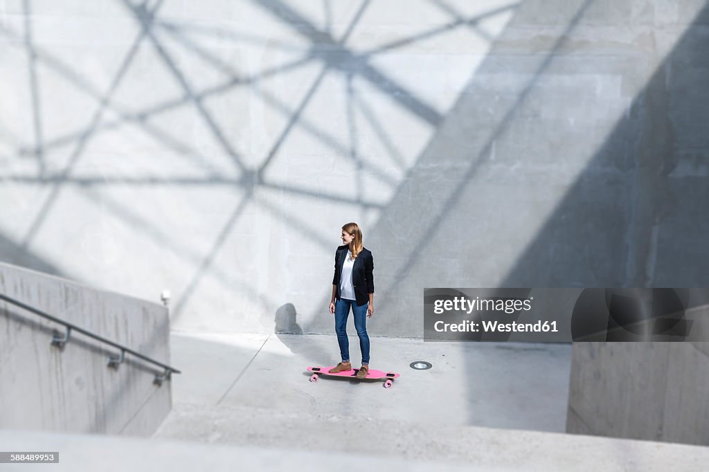 Businesswoman with pink skateboard in modern architecture