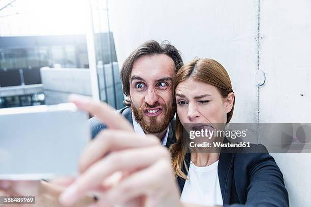 portrait of two business people making faces while taking a selfie with smartphone - scheel kijken stockfoto's en -beelden