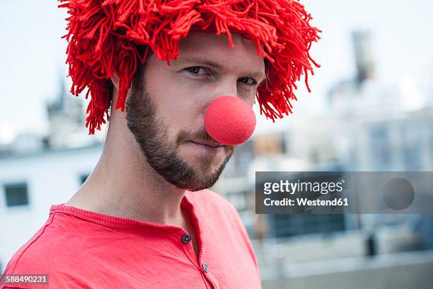 germany, cologne, portrait of bearded young man wearing clown's nose and red wig - clownsneus stockfoto's en -beelden