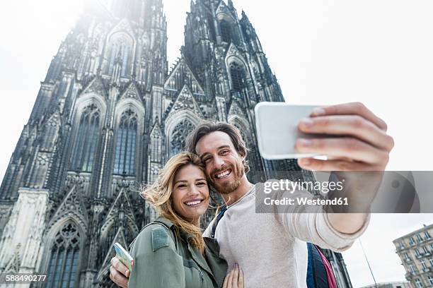 germany, cologne, portrait of young couple taking a selfie in front of cologne cathedral - tourist selfie stock pictures, royalty-free photos & images