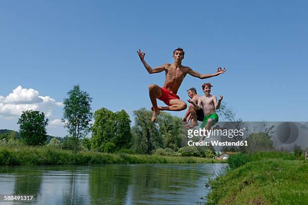 germany, bavaria, two teenage boys and man jumping into river loisach - yoga teen stock pictures, royalty-free photos & images